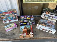 Various boxed jigsaw puzzles displayed on a surface including American Landscape 10-pack, fantasy warrior puzzle, and other boxed puzzles.
