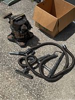 Full view of Rainbow vacuum cleaner with several attached hoses and cleaning attachments on the ground with a cardboard box nearby.