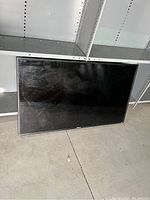 Front view of Roku TV laid flat on concrete floor, screen off, showing some smudges and reflections.
