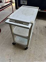 Full view of white plastic rolling utility cart showing top shelf, middle shelf, base shelf, and four caster wheels.