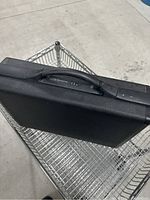 Black Samsonite briefcase with combination lock visible, placed on a metal shopping cart.