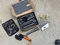 Full kit with all components displayed: metal multi-functional shovel head, handle pieces, small axe with orange handle wrap, and camouflage pouch.