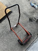 Small two-wheel dolly converted to cart configuration shown on textured concrete surface, highlighting frame, handlebar, and wheels.