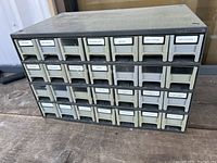Front view of plastic tool tray box with 24 small drawers arranged in three rows. Drawers have labels with names of hardware types.