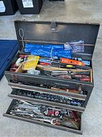 Open metal Craftsman toolbox displaying various hand tools organized in top compartment and two drawers.