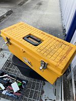 Yellow plastic toolbox closed on a cart outdoors with visible markings and some rust on top