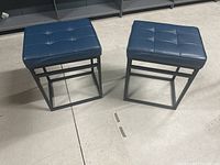 Two blue upholstered barstools side by side on a concrete floor, showing overall condition and design.