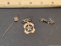 Three antique gold pins displayed on black background with a ruler above for scale, showing the size of each pin.