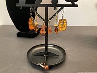 Three pairs of amber earrings displayed on a black metal holder. Varied styles including rectangular amber, small amber beads with silver accents, and amber chip beads.