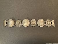 Full view of the antique bracelet showing Colombian coins and silver panel links on a black background.