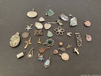 Photo showing a variety of silver pendants on a dark surface, highlighting different shapes and embedded stones.