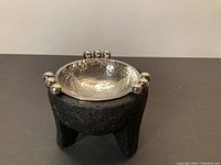 Front view of the molcajete showing the lava stone legs and silver bowl with decorative silver spheres.