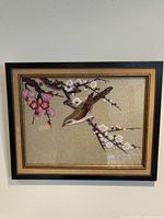Framed hand embroidered wall art showing a bird on branches with white and pink blossoms.