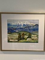 Framed watercolour painting showing a landscape of mountain range with green hills and trees, signed by artist.
