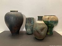 Set of four Raku pottery vases arranged in a row showing varied shapes and glaze colors.