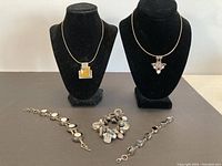 Overview of two necklaces with pendants displayed on black stands and three silver bracelets laid out on surface.