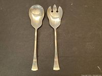 Two sterling silver serving utensils: a serving spoon and a serving fork, side by side showing bowl and tines.