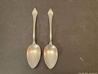 Full view of two sterling silver serving spoons side by side on a dark background.