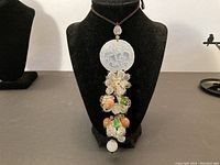 Full view of necklace with carved circular stone pendant and clusters of jade, crystal, and various colored stones on a black jewelry bust.