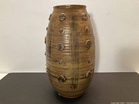 Oval ceramic vase with brown finish and raised circular details on sides, placed on flat black surface.