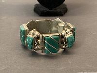 Front view of vintage heavy sterling silver bracelet with turquoise stones, showing carved rectangular and triangular turquoise pieces with silver inlays and decorative silver bead accents.