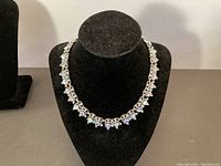 Front view of vintage Trifari necklace on black velvet display, showing silver tone metal and aurora borealis rhinestones.