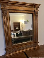 Full view of antiqued gold/bronze framed mirror, showing ornate carved details on the frame and reflection of room.