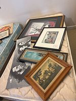 Framed artworks and photographs arranged on a mattress including portraits, abstract print and cityscape artwork.