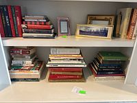 Photo of bookshelf with stacks of books and framed pictures on the middle shelf.