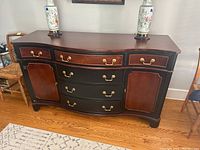 Front view of the wood buffet showing three upper drawers with brass handles, two curved front drawers in the center, and two side cabinet doors with light scratches and brass hardware.
