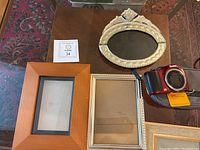 Photo shows six picture frames of various finishes and two Kodak cameras with their cases on a dark wooden surface.