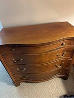 Front angle view showing the four drawers with brass handles and knobs, highlighting the wavy drawer fronts and wood finish.