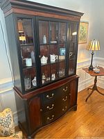 Full front view of the black and brown china hutch showing upper glass display cabinets with contents and lower drawers and cabinets.