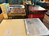 Photo showing ten coffee table books stacked and laid on glass table, including The Big Book of How to Say It, And The Fans Roared, Konditoreibuch, In Focus, Herboldsheim, Science, and an empty card holder book with plastic sleeves seen open.