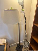 Two floor lamps standing next to each other; one with white fabric shade and square base, the other with curved metal stand and frosted glass shades.