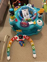 Baby Einstein activity gym with attached toys and brightly colored bouncy seat with removable toy arch on beige carpeted floor.