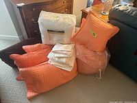 Complete set of king size bedding items including an orange comforter, pillows, white sheets, and mattress pad.