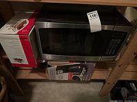 Insignia microwave on wooden shelf with boxed Cuisine Select 3-piece serving dish alongside.