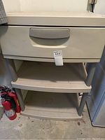 Plastic storage unit with one drawer and three shelves in beige plastic, showing front view.