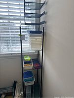 Full view of black metal 5-tier shelving unit holding assorted plastic bins and trays