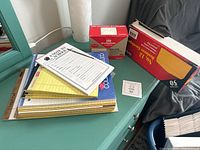 Stack of mixed notepads, unopened box of business envelopes, and unopened box of invitation envelopes on desk.