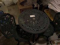 View of round green metal patio table and two matching chairs, all with detailed floral cut-out designs.
