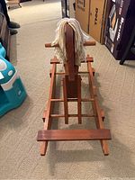 Front view of the handmade wooden rocking horse showing the seat area, wooden body, and white yarn mane.