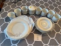 Full view of 6 tea cups, 6 saucers, sugar bowl with lid, creamer, and 6 dessert plates on a patterned tablecloth.