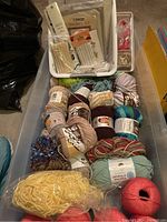 Photo showing yarn skeins and balls in a plastic bin along with a plastic tray containing stitching and craft supplies