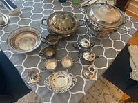 Overview of the various silver plate serveware items laid out on a table including covered serving dishes, sugar and creamer set, teapot, and candle holders.