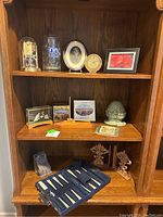 Full shelf view showing all items including clocks, glass stein, framed photos, decorative sculptures, postcards, carved trees, and backgammon set
