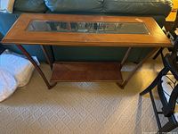 Full view of the sofa table showing the wood frame, brass accents, glass inset tabletop, and lower shelf.