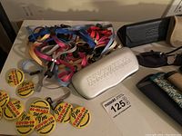 Photo showing multiple colorful glasses lanyards, yellow Covid-19 vaccination pins, and a silver Innoluvr hard case.