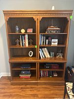 Front view of the pair of oak wood Thomasville bookcases filled with books and decorative items.